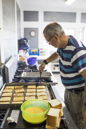 Elderly man cooking french toast in industrial kitchen.