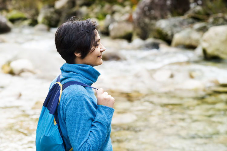 Side view of smiling woman standing on riverbank in forest