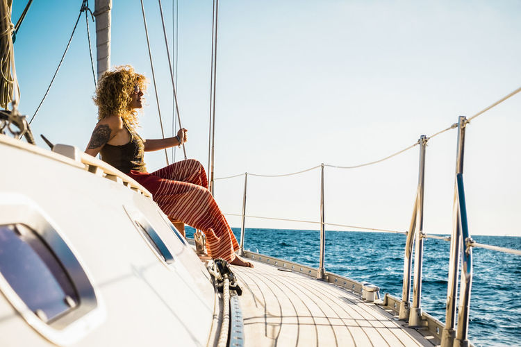 Woman sitting on sailboat in sea against sky