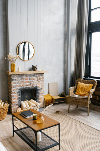 A coffee table by the fireplace of a country house and a wicker chair in the living room 