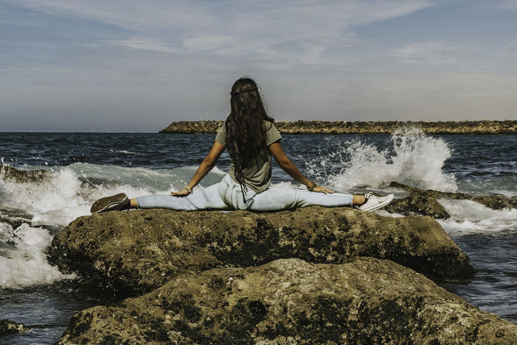 A young women yoga pose on rock at sea shore against sky