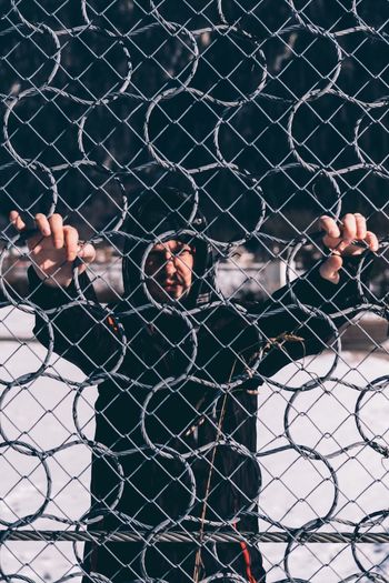Full length of man seen through chainlink fence