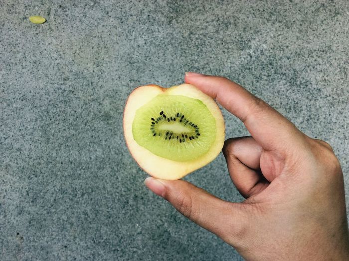 Cropped image of hand holding apple with kiwi
