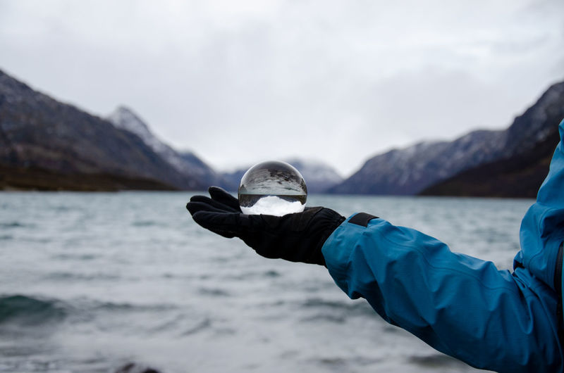 Hiker holding a glass sphere mirroring the mountains enclosing the gjende lake