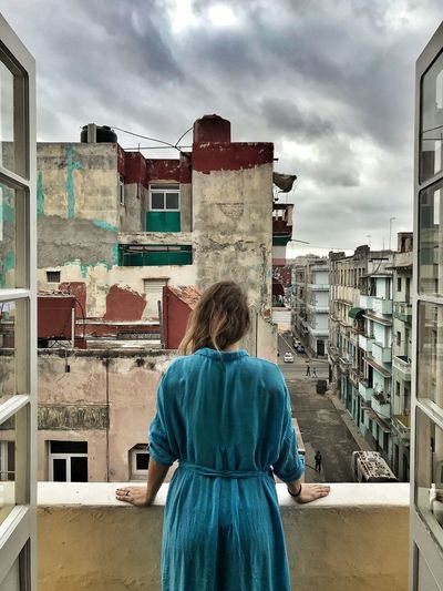 Rear view of mid adult woman standing in balcony against cloudy sky