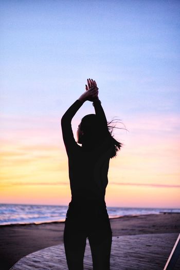 Woman standing at beach against sky during sunset