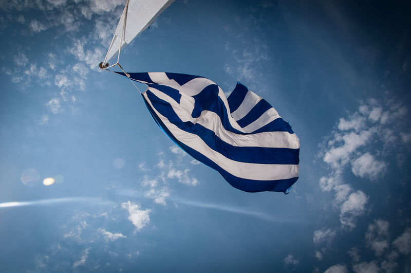 Low angle view of greek flag fluttering against blue sky