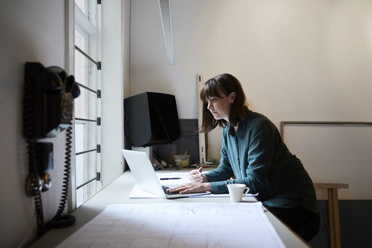 Confident female architect using laptop in office