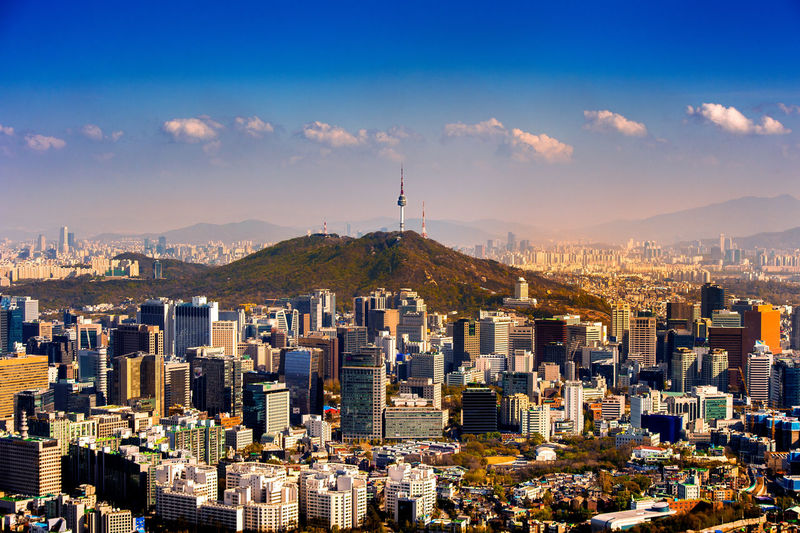 Distant view of n seoul tower on namsan mountain amidst cityscape against sky