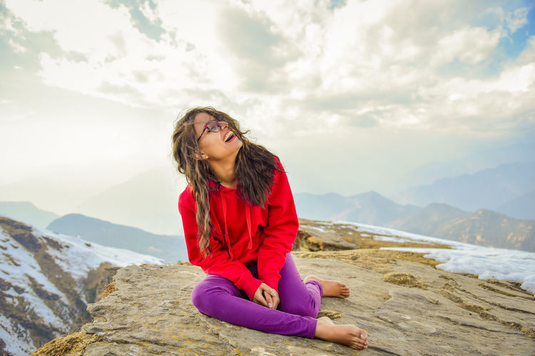 Happy young woman sitting on mountain against sky