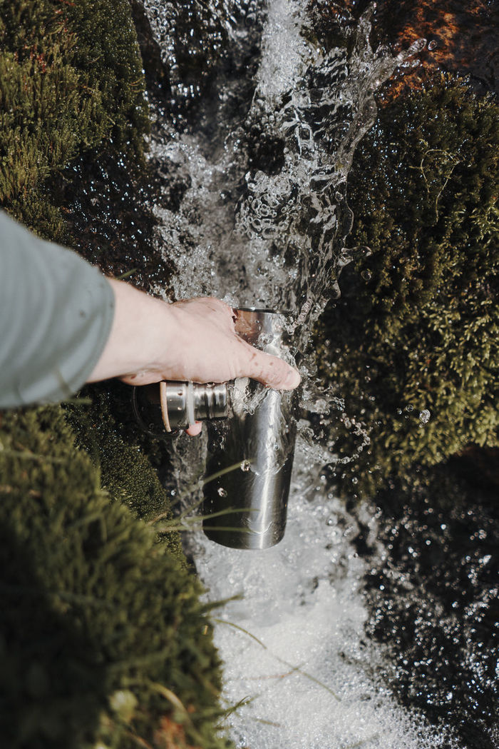 High angle view of person hand holding bottle in waterfall by rock