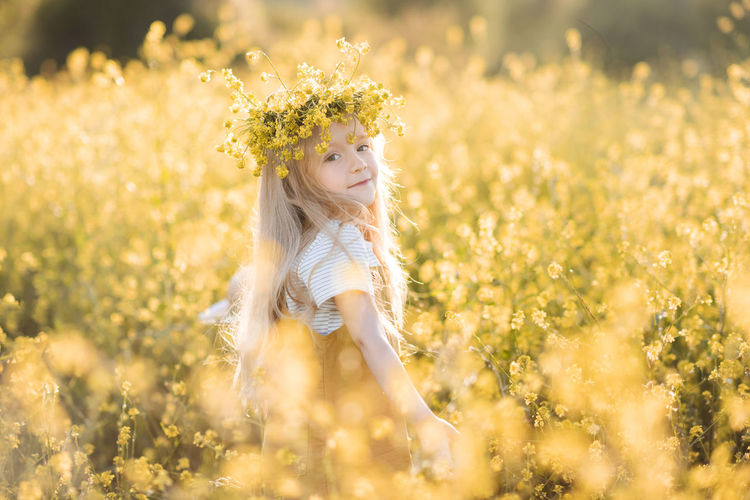 Cute child girl 4-5 year old wear floral wreath stand in yellow flower meadow outdoor over nature