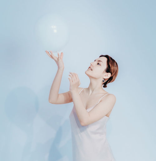 Portrait of smiling young woman blowing bubbles against blue background