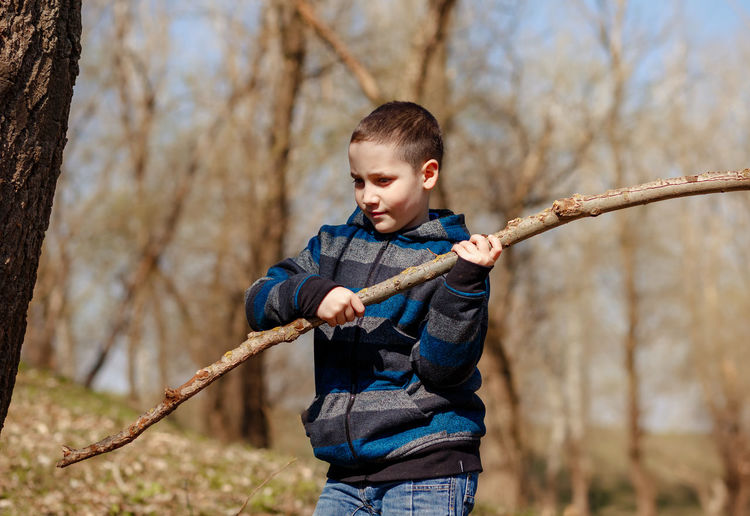 Boy holding stick against trees outdoors