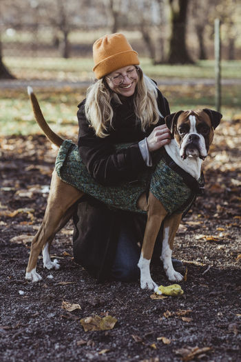Smiling young woman looking at boxer dog while kneeling