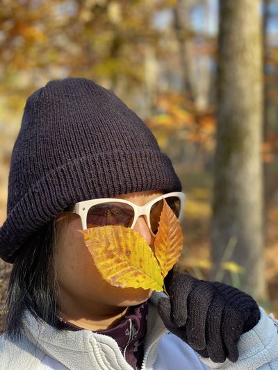 Close-up of woman wearing sunglasses holding autumn leaves