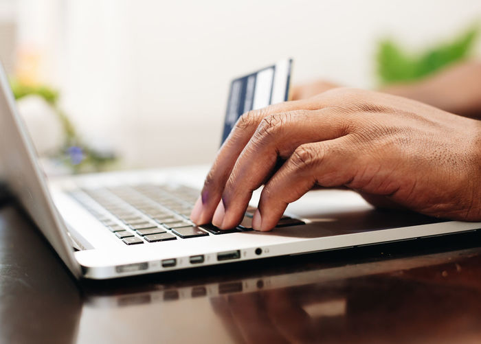 African american man at home using laptop computer to shop online with credit card in hand