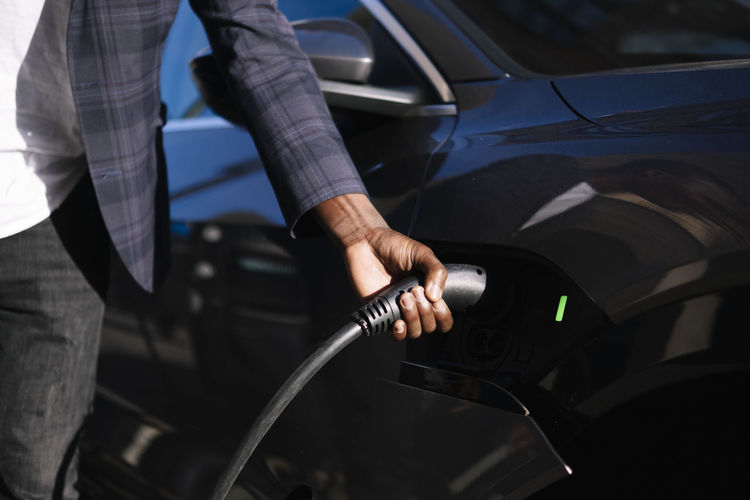 Hand of man plugging charger into electric car