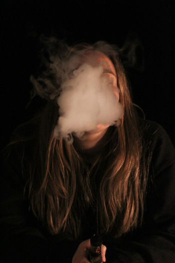 Woman exhaling smoke against black background