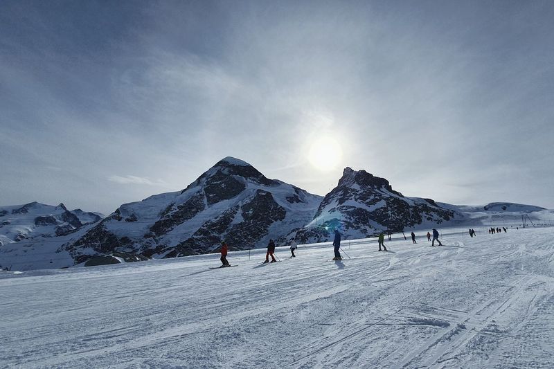 People skiing on snow covered land during winter against sky