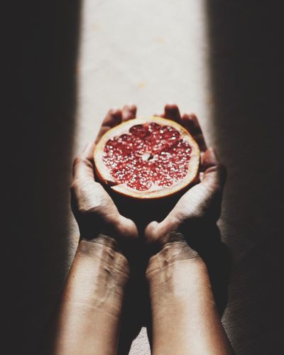 Cropped image of person holding halved grapefruit in sunlight