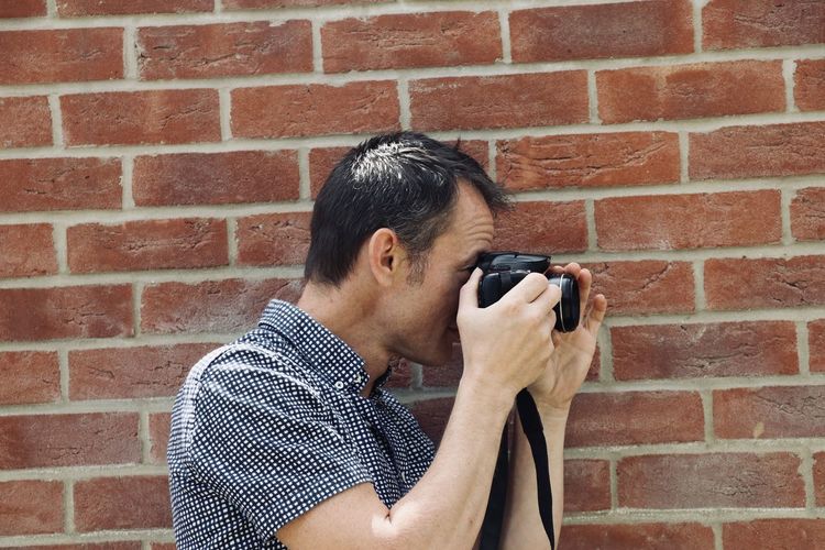 Man photographing against brick wall