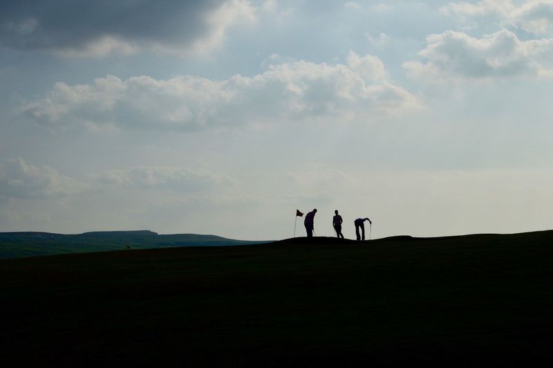 Silhouette friends playing golf on field against sky