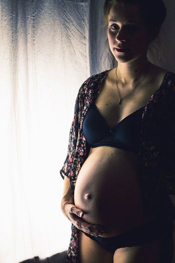 Portrait of pregnant woman standing by window at home