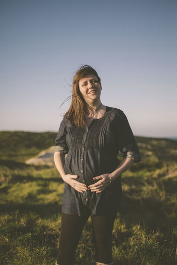 Happy pregnant woman standing on field against clear sky