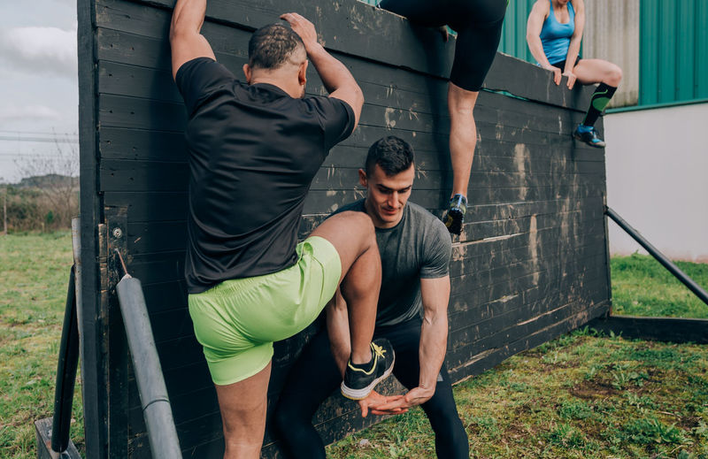 Man helping friend in climbing wooden wall while exercising