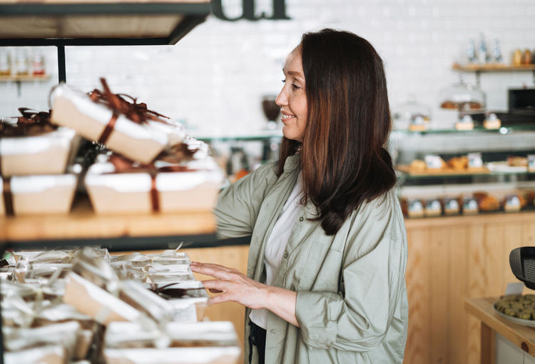 Adult smiling brunette woman forty years with long hair in stylish shirt choosing sweets in cafe