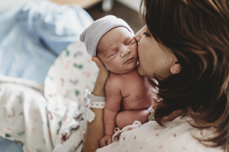 Close up detail of mother kissing newborn son's cheek in hospital negative space