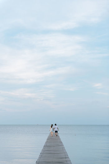 Mid adult couple walking on jetty over sea