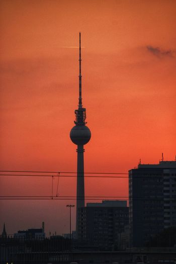 Communications tower in city against romantic sky at sunset