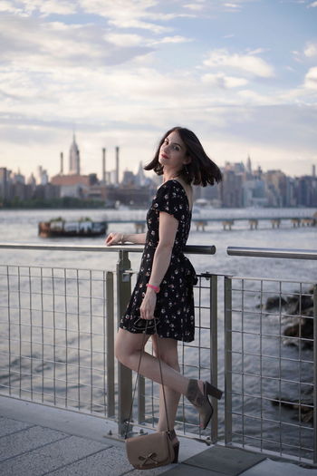 Full length portrait of young woman standing by river at manhattan