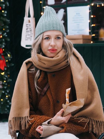 Young woman with blonde hair wearing brown fur coat eating sweet food on the christmas market.