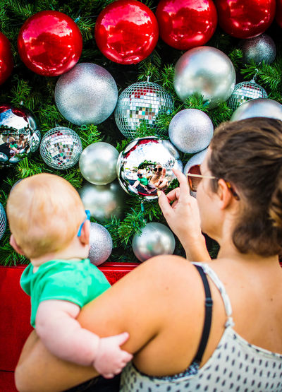 Rear view of mother carrying son while touching christmas bauble on tree
