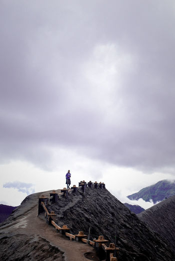 Hiker standing on mountain against cloudy sky