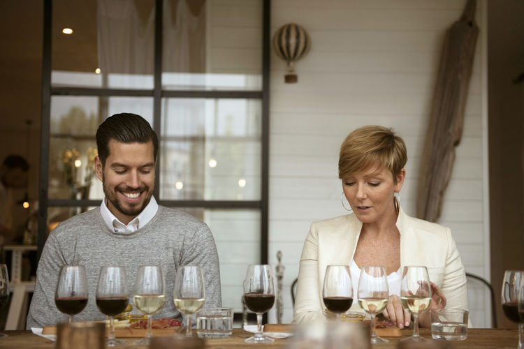 Smiling business people analyzing wine glasses while sitting at table