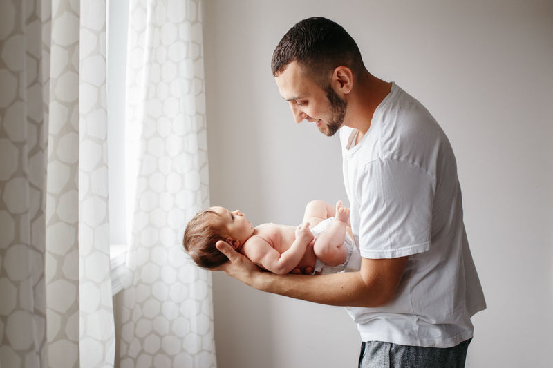 Side view of father carrying baby daughter against wall at home