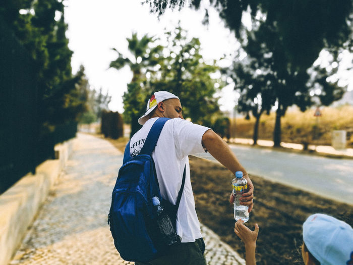 Mid adult man giving water bottle to son on sidewalk