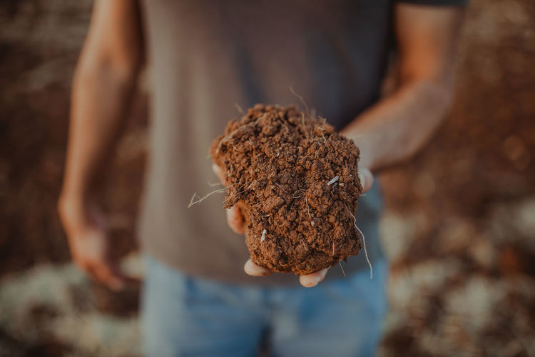 Midsection of man holding soil while standing on field