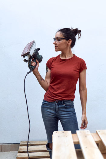 Young woman with a power sander on a white background.