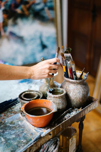 Anonymous female artist taking paintbrush from pot with various brushes in art workshop
