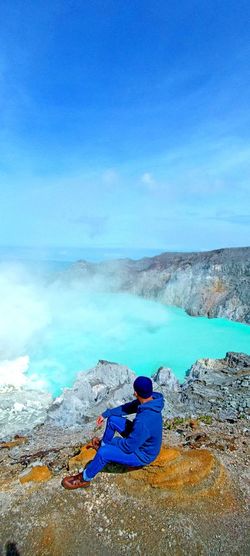 Rear view of man sitting on the top of the ijen mountain enjoying the magnificent turquoise crater.