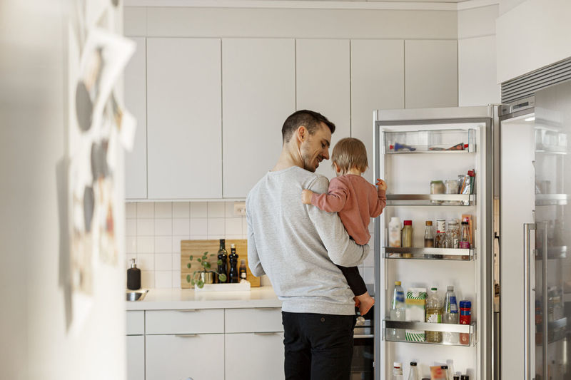 Father carrying toddler daughter in kitchen