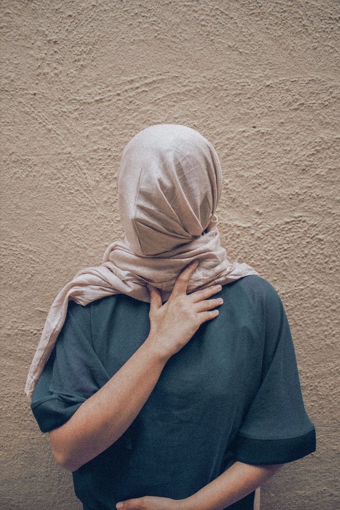 Woman covering face with scarf against wall