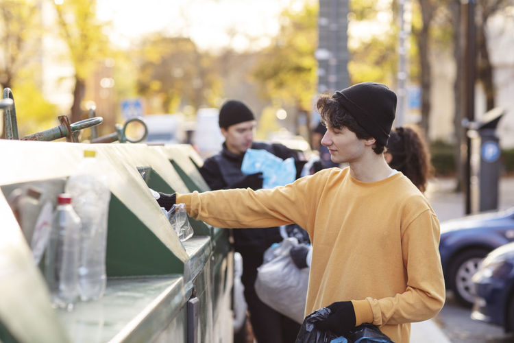 Smiling male environmentalist throwing plastic waste in garbage can