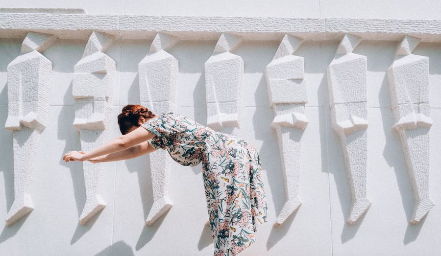Side view of woman bending by white wall during sunny day