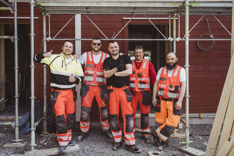 Full length of smiling male construction workers standing together at site